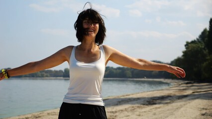 Beautiful lady walking on sandy beach near shoreline at sunny day. Happy adult woman turning around near coastline. Carefree female enjoying rest at seaside. Concept of summer vacation or holiday