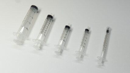 Five disposable plastic syringes without needles arranged diagonally on a white background. The...