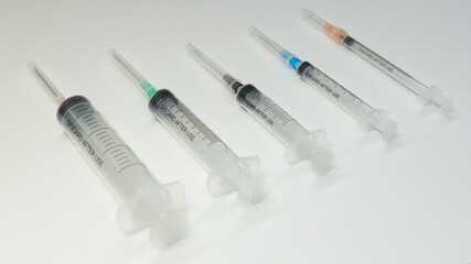 A set of sterile medical syringes arranged diagonally on a white surface. Each syringe has a...