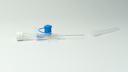 IV cannula with blue valve and exposed needle placed next to its transparent protective cap on a white background.