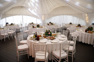 Elegant indoor event setting featuring round tables with white linens and arranged floral...