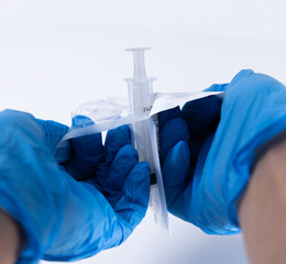 Close-up of gloved hands opening the sterile packaging of a disposable syringe. Essential...