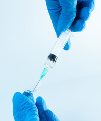 Gloved hands drawing liquid medication from an open glass ampoule using a syringe. Sterile medical...