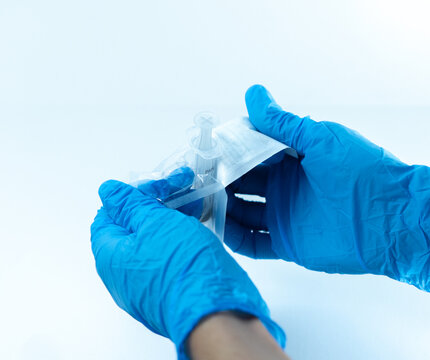 Wide-angle view of gloved hands opening a disposable syringe from its sterile blister packaging. Sterile medical preparation in clinical or hospital setting.