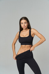 Athletic woman in black activewear poses confidently, revealing toned abs while pulling her...