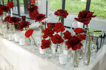 Stunning event table setup features vibrant red roses in glass vases, surrounded by numerous white...
