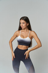 Fit woman in ombre sportswear posing confidently with hands on hips. She wears a gradient sports...