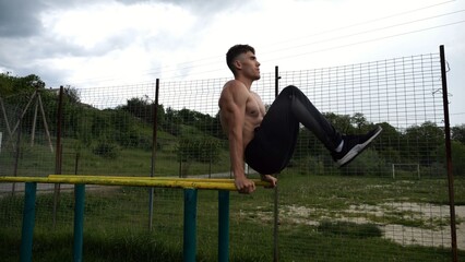 Strong guy training abdominal muscles on parallel bars at sports ground. Young shirtless sportsman...