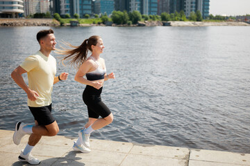 Couple jogging together by the riverfront on a sunny day, enjoying fitness and fresh air in a vibrant urban setting
