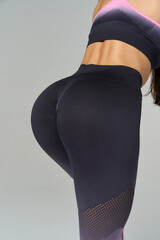 Fit woman in athletic outfit, showcasing a toned back and legs. She is wearing dark leggings with mesh details and a pink-patterned sports top, highlighting fitness and an active lifestyle