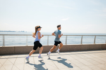 Couple jogging along waterfront promenade on sunny day, enjoying exercise and each other's company...