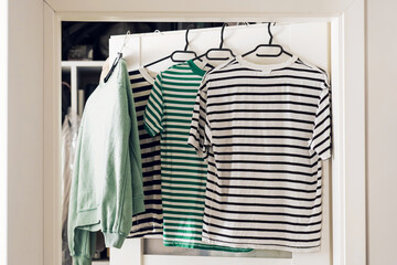 Clothes hanging on hanger in doorway. Striped t-shirts and green sweatshirt drying indoors. Laundry...