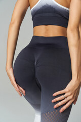 Athletic woman in two-tone sportswear, hands rested on dark gray leggings with textured detail, showcasing fit physique. Cropped top, ring visible, focus on workout apparel style