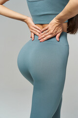 Hands resting on lower back, person in ribbed teal activewear outfit. The focus is on posture and clothing texture, emphasizing health and fashion aspects. Long hair partially visible