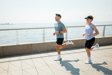 Jogging along the waterfront promenade in bright sunlight, two fitness enthusiasts embrace the morning energy of their daily run