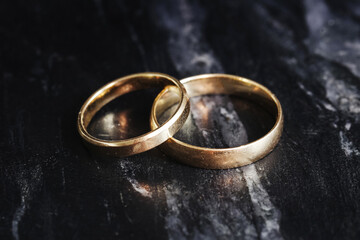 Two simple gold wedding rings. Symbol of love and commitment. Closeup of golden bands on dark...