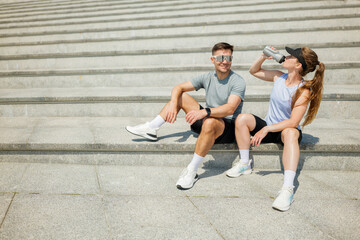 Friends enjoying a refreshing break while exercising on outdoor steps in sunny weather