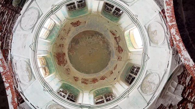 View from below dome of an abandoned Christian church made of red brick and plaster. On ceiling, there are traces of destroyed fresco depicting faces of saints and Jesus Christ.