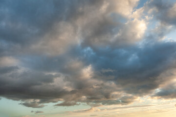 Obraz premium Majestic cloud formations during sunset casting shadows across the vibrant sky above a tranquil landscape