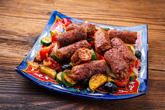 Traditional Croatian cevapcici spicy meat ball rolls with troasted vegetables served as close-up on a rustic design plate