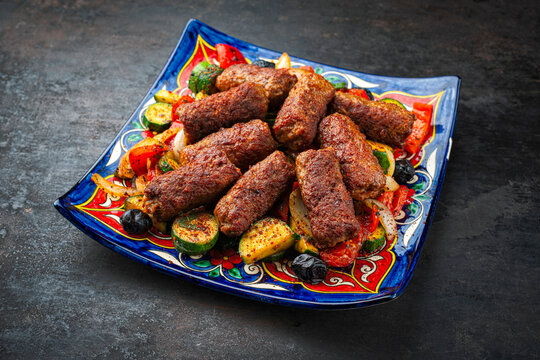 Traditional Croatian cevapcici spicy meat ball rolls with troasted vegetables served as close-up on rustic plate