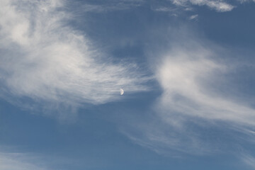Clouds drift softly in the blue sky as the crescent moon appears during late afternoon