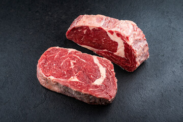 Dry aged raw beef entrecote cuts with fat marbling offered as close-up on a black rustic board