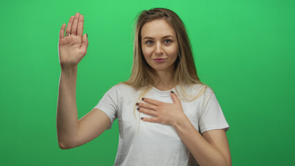 Woman raising hand in a pledge gesture standing against a green isolated background wearing a white...