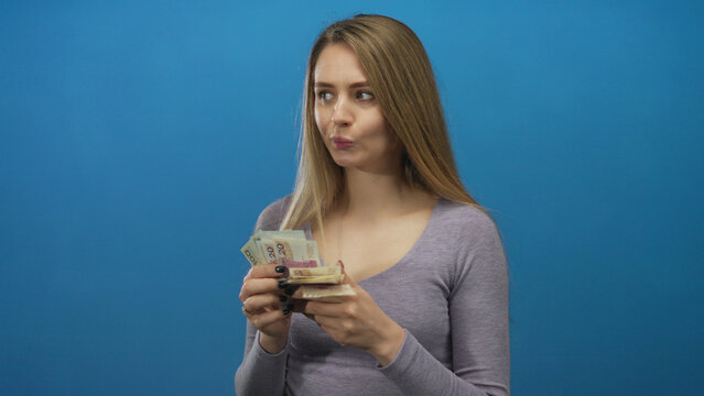 Young woman counting polish zloty banknotes against an isolated blue background, illustrating financial management and currency handling.