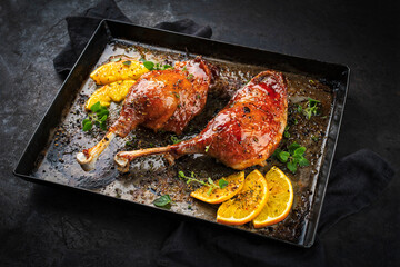 Traditional barbecue gourmet duck haunch with orange slices and herbs served as close-up on a rustic metal tray