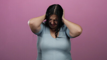Woman with closed eyes covers ears in stress isolated against vibrant pink wall suggesting...