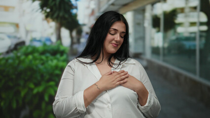 Woman in white shirt, standing confidently on a sunny city street, expresses contentment and...