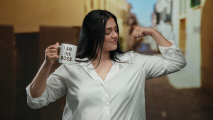 Confident woman in white shirt poses with mug reading 'i am the boss' flexing on a city street,...