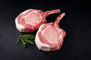 Raw dry aged trimmed bone-in pork loin chops cutlets offered as close-up on a black board