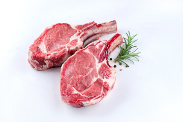 Raw dry aged bone-in back veal chops offered as close-up with herbs and spice on white background