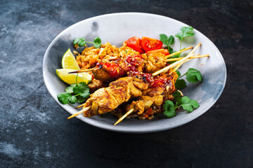 Authentic Sate Ayam - grilled chicken satay sate skewers with stir-fried rice and vegetable served as close-up in a design plate