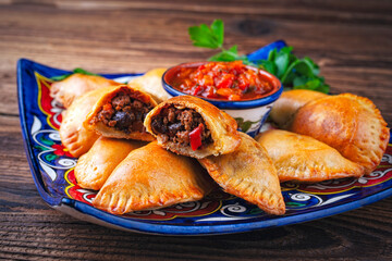 Artisan Argentinian homemade empanadas with minced meat and salsa dip served as close-up on a traditional plate