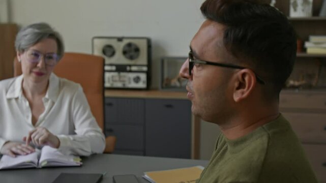 Middle aged female psychotherapist talking to adult Indian man helping building dialogue with spouse during family therapy session at modern office