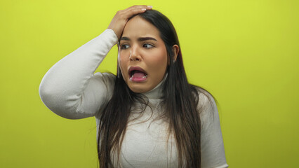 Young hispanic woman over isolated yellow background expressing surprise with hand on face showing...