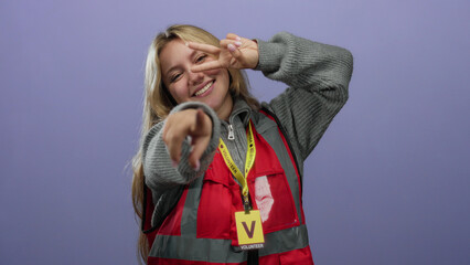 Woman smiling volunteer pointing in red vest with purple background isolated showing enthusiasm and...