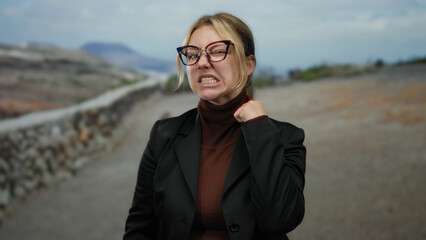 Young blonde woman in glasses making vigilant and threatening gestures in a park setting,...
