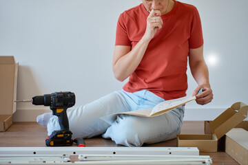 Woman sitting on floor reading instruction manual during furniture assembling. Person sitting on...
