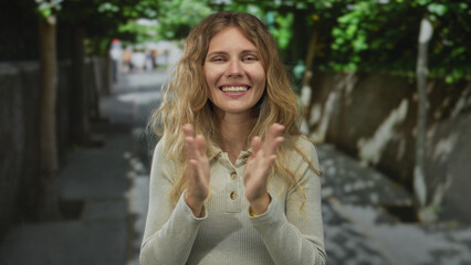 Woman raises her hands clapping on a street with a blonde smiling expression in an outdoor urban...