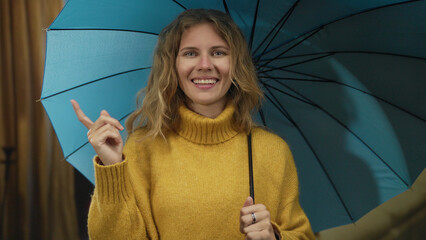 Woman uses umbrella while smiling indoors as blonde young figure in yellow sweater lifts finger to...