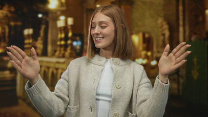 Woman smiling with raised hands inside a dimly lit church, showcasing youthful expression and...