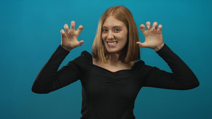 Blonde woman playfully gesturing against a vibrant blue background, expressing happiness and...