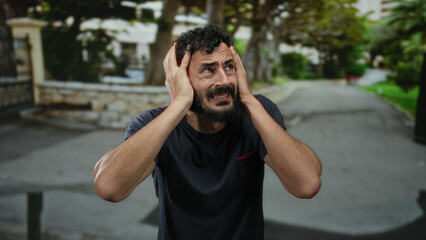 Hispanic man with beard looking distressed on an outdoor street, surrounded by blurred trees and...