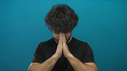 Young man meditating with hands in prayer against a serene blue background conveying peace and...