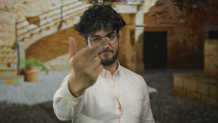 Young bearded man outdoors on sunny day making rude gesture showing middle finger in courtyard with...