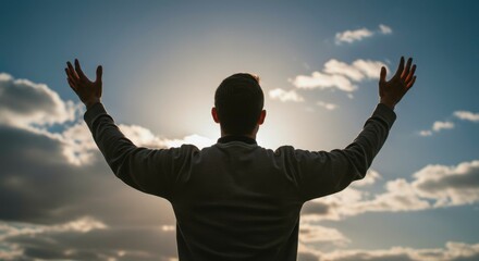 Silhouetted man with arms raised high, basking in sunlight against a partly cloudy sky